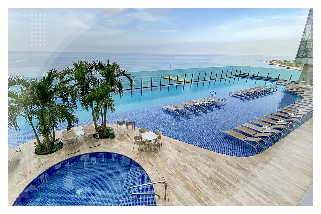 Piscina infinita con vista al mar, rodeada de palmeras, sillas asoleadoras y una zona húmeda de descanso, ideal para disfrutar en los exclusivos Hoteles Estelar de Cartagena.