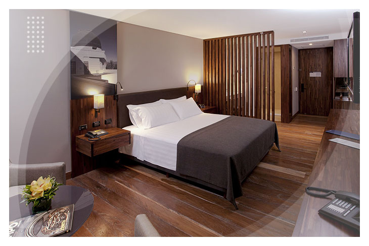 Habitación con cama doble, sábanas blancas, piso en madera y muebles de estilo moderno, en uno de los espacios diseñados para el descanso en los Hoteles Estelar de Bogotá.