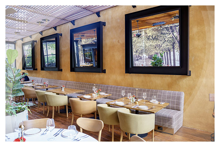 Restaurante con mesas de madera junto a una pared con ventanas amplias, sillas modernas y decoración acogedora en uno de los espacios gastronómicos que puedes disfrutar en los Hoteles con descuento de la Calle 93.