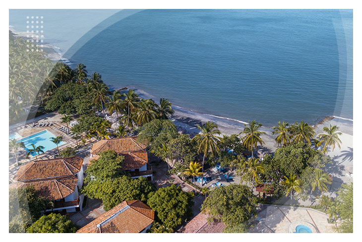 Vista aérea del hotel que tiene techos de teja color rojo rodeados de palmeras, con acceso directo a la playa y zonas húmedas, una opción perfecta de los hoteles en Santa Marta con descuento.