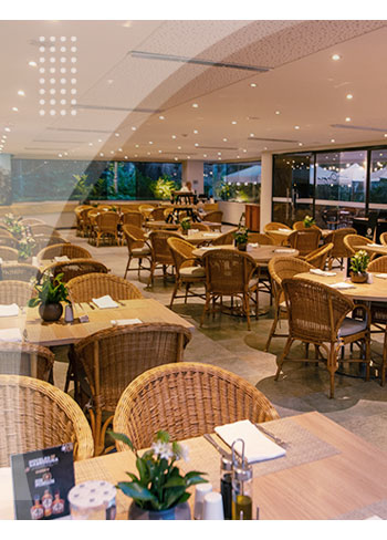 Espacioso restaurante con múltiples mesas y sillas de mimbre, rodeado de ventanales que permiten ver zonas verdes, como parte de los servicios de los mejores hoteles en Santa Marta.