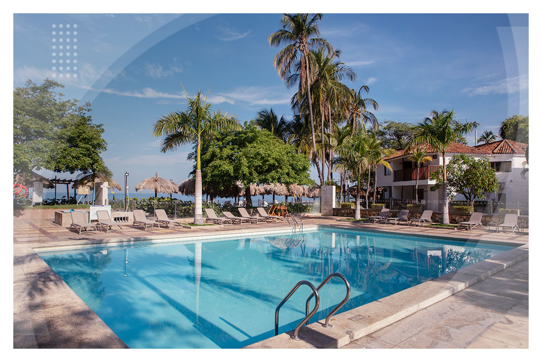 Piscina con sillas asoleadoras rodeada de palmeras y zonas verdes ideal para descansar y disfrutar en uno de los hoteles en Santa Marta cerca al mar.