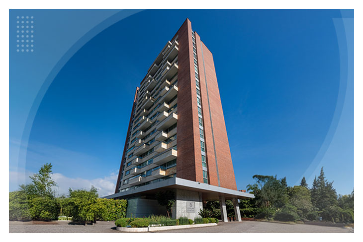 Gran torre con amplios balcones, rodeada de zonas verdes y un cielo completamente azul, que hace parte del exclusivo Hotel Estelar La Torre Suites Medellín
