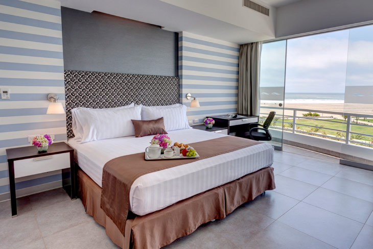 Habitación amplia y luminosa con cama doble, decoración en tonos neutros y balcón con vista al océano, ideal dentro de los planes hoteleros Estelar Perú