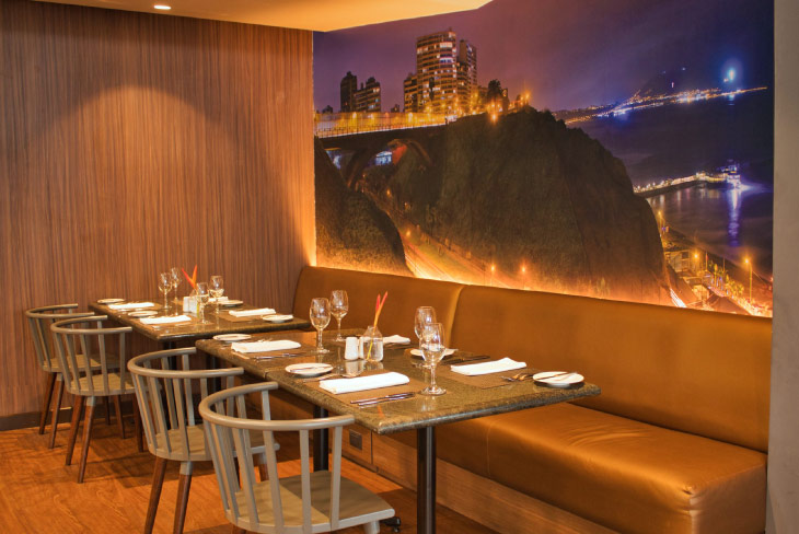 Restaurante elegante con mesas montadas y mural nocturno de ciudad, una experiencia gastronómica incluida en los planes turísticos de los hoteles Estelar Lima