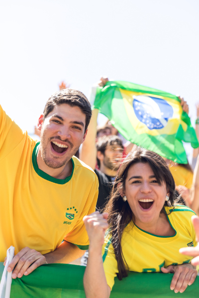 Aficionados con camisetas de Brasil celebrando y levantando la bandera nacional, representando la emoción del paquete de viaje para São Paulo durante un ambiente deportivo internacional